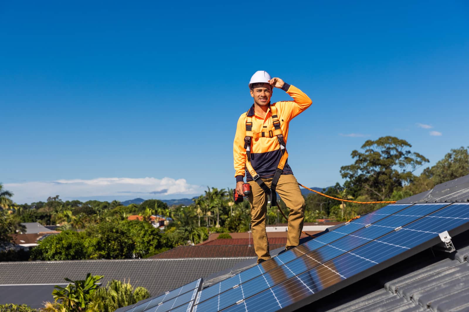 A Solar water wind employee standing on top of a roof next to the solar panels he has installed